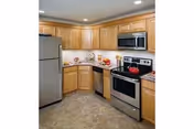 Modern kitchen with stainless steel refrigerator, stove, microwave and dishwasher, light wood cabinets, and tiled floor.