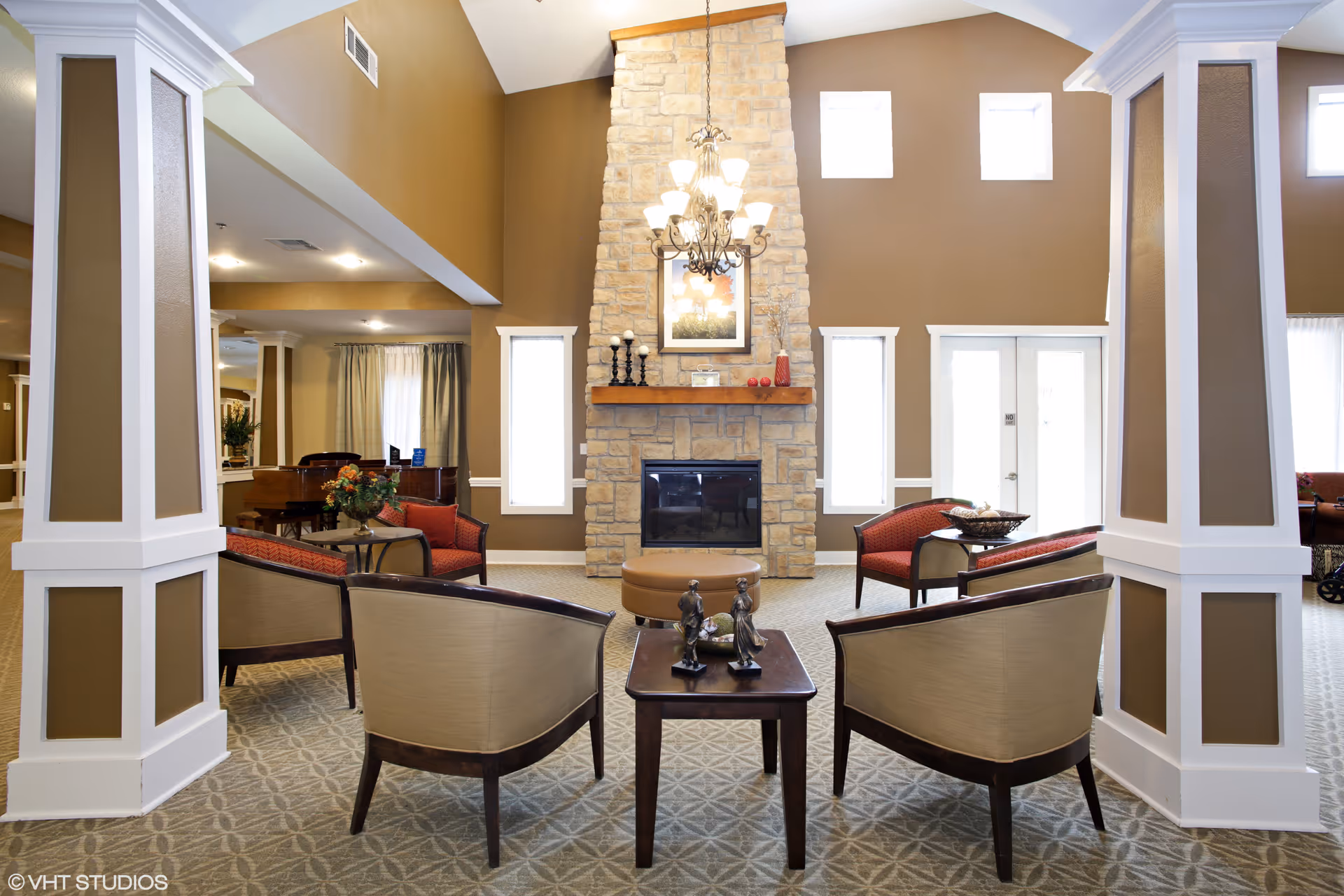 Bright common lounge with chairs and tables arranged around a stone fireplace beneath a chandelier.