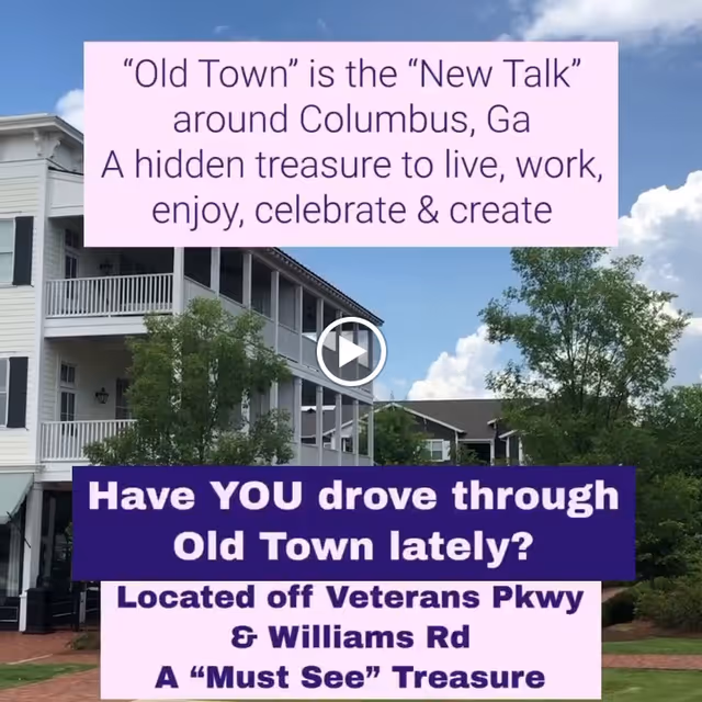 Exterior view of a multi-story residential building with white siding and balconies, surrounded by trees and greenery under a partly cloudy sky. Text overlays describe Old Town in Columbus, GA as a hidden treasure to live, work, enjoy, celebrate, and create, and invite viewers to visit the area located off Veterans Parkway and Williams Road.