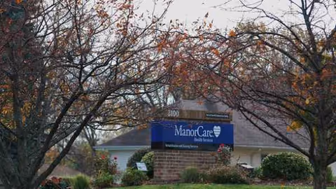 Exterior view of The ManorCare entrance at Kenosha with a sign and trees.