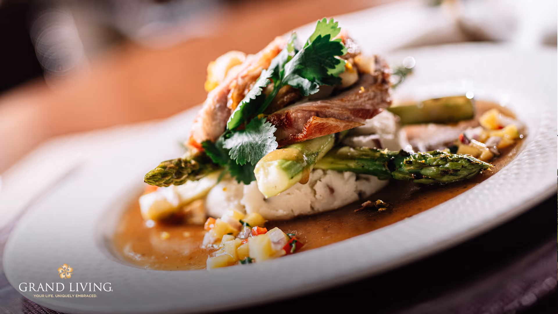 Close-up of a plated gourmet dish with asparagus, mashed potatoes, sliced meat, and sauce.