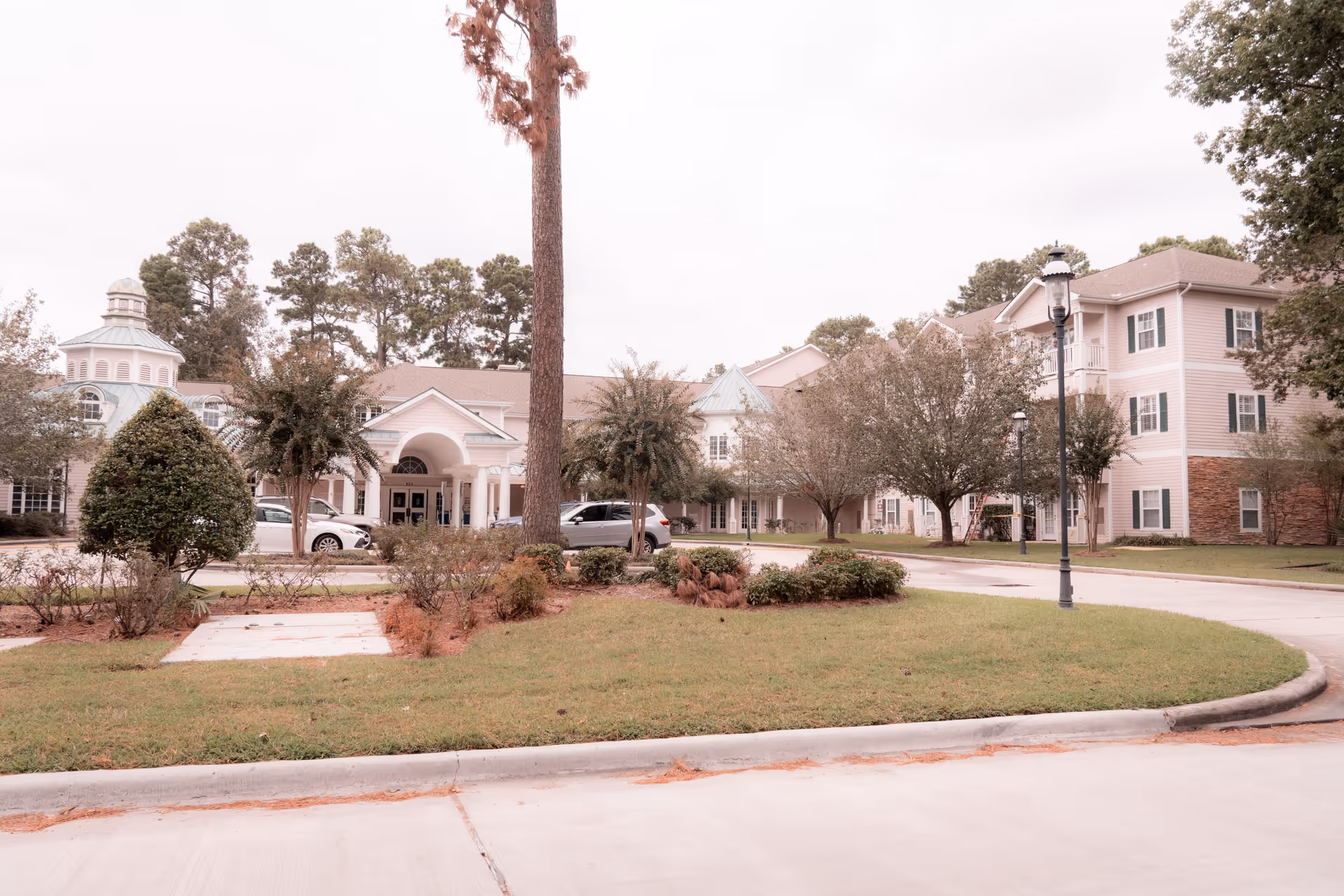 Front exterior of a senior living facility with a circular driveway, landscaped lawn, and multi-story building.