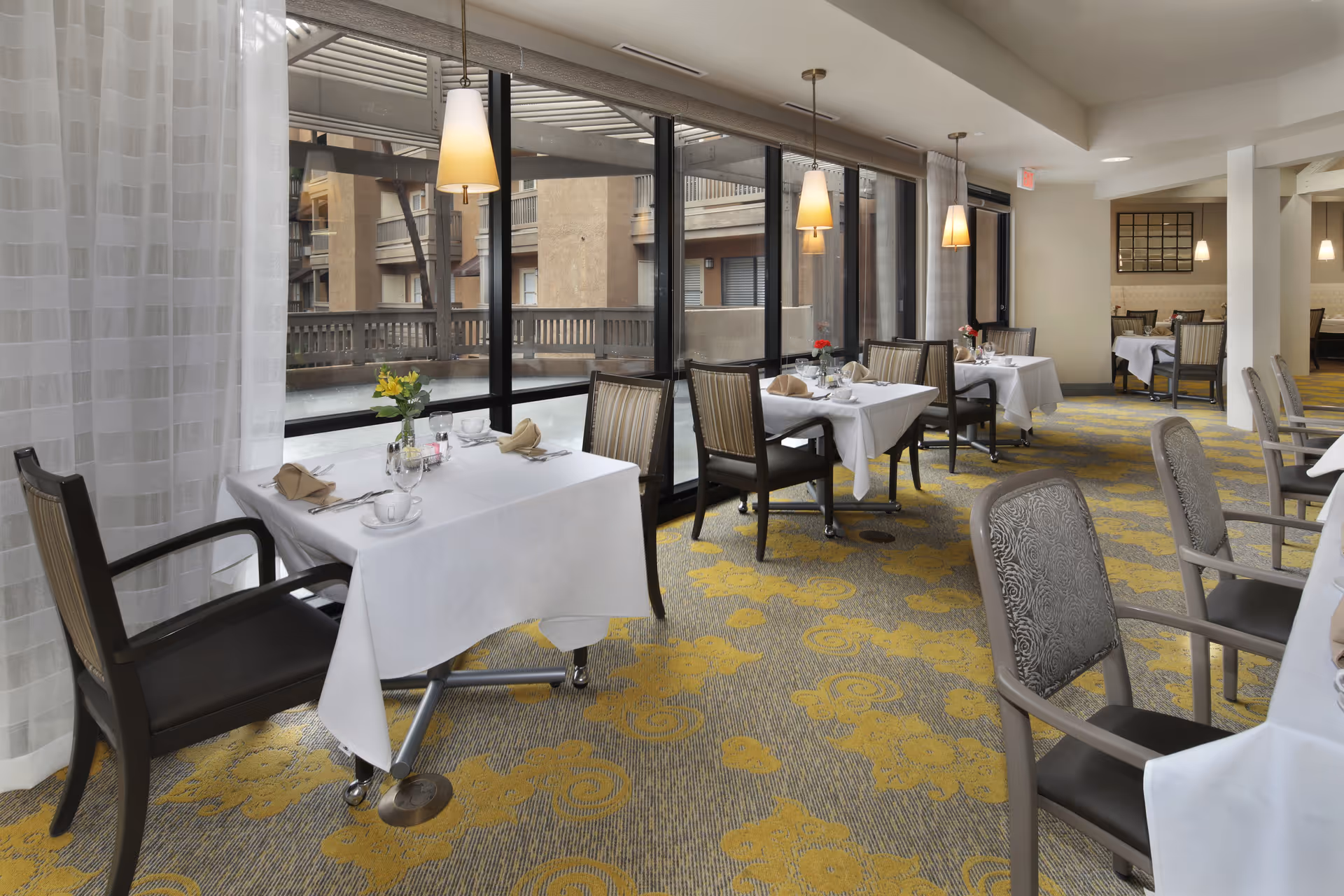 Dining room with several set tables and chairs beside large windows and pendant lights.