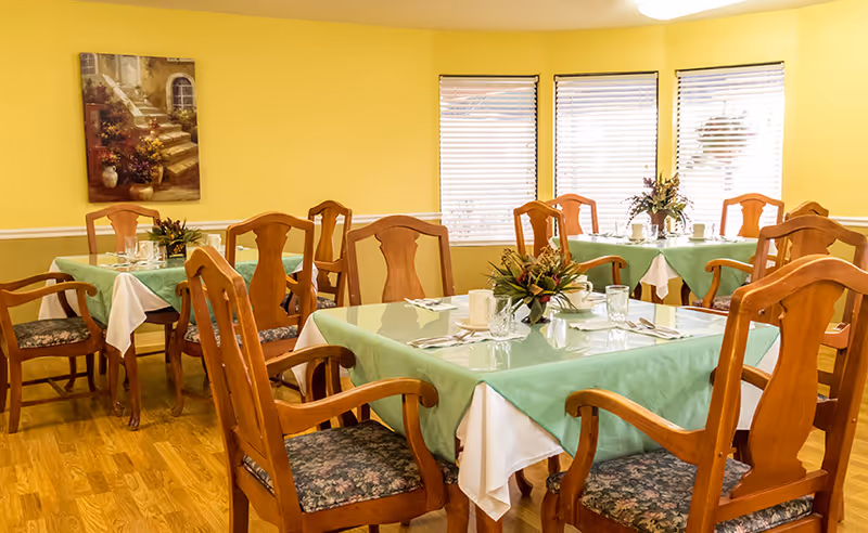 Dining room with wooden tables and chairs set with green tablecloths, place settings, and floral centerpieces.