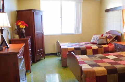 Two twin beds with patchwork quilts flank a dresser and wardrobe under a window.