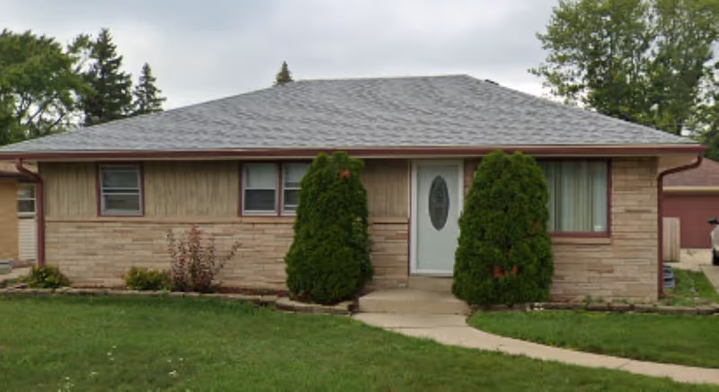 Single-story brick senior home with curved walkway, two evergreen shrubs, and a front door.