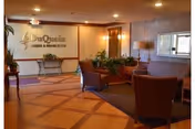 Interior view of a reception or lobby area at Fairview Rehabilitation & Healthcare featuring a seating area with chairs and a small table, plants, a large mirror on the wall, and a sign with the facility's name on the back wall.