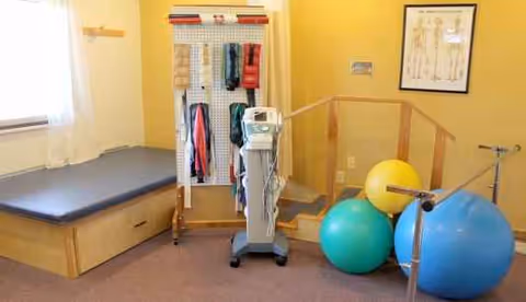 Interior therapy room with exercise equipment, a bench, towels rack, and blue and yellow exercise balls.