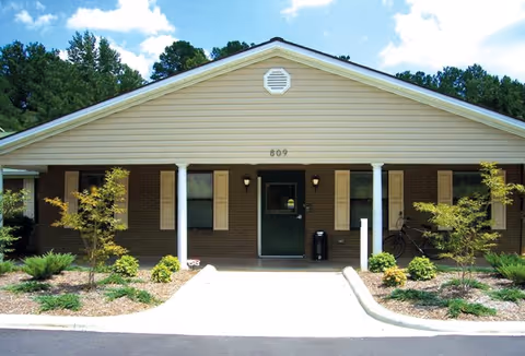 Front view of a single-story brick senior living facility with two columns and landscaped entrance.