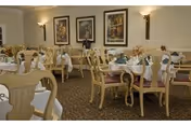 Well-lit dining room with multiple tables set with napkins and chairs, decorated with framed artwork and wall sconces.