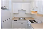 Small kitchen with white cabinets, a white refrigerator, a white electric stove with four burners, a stainless steel sink, and beige countertops.