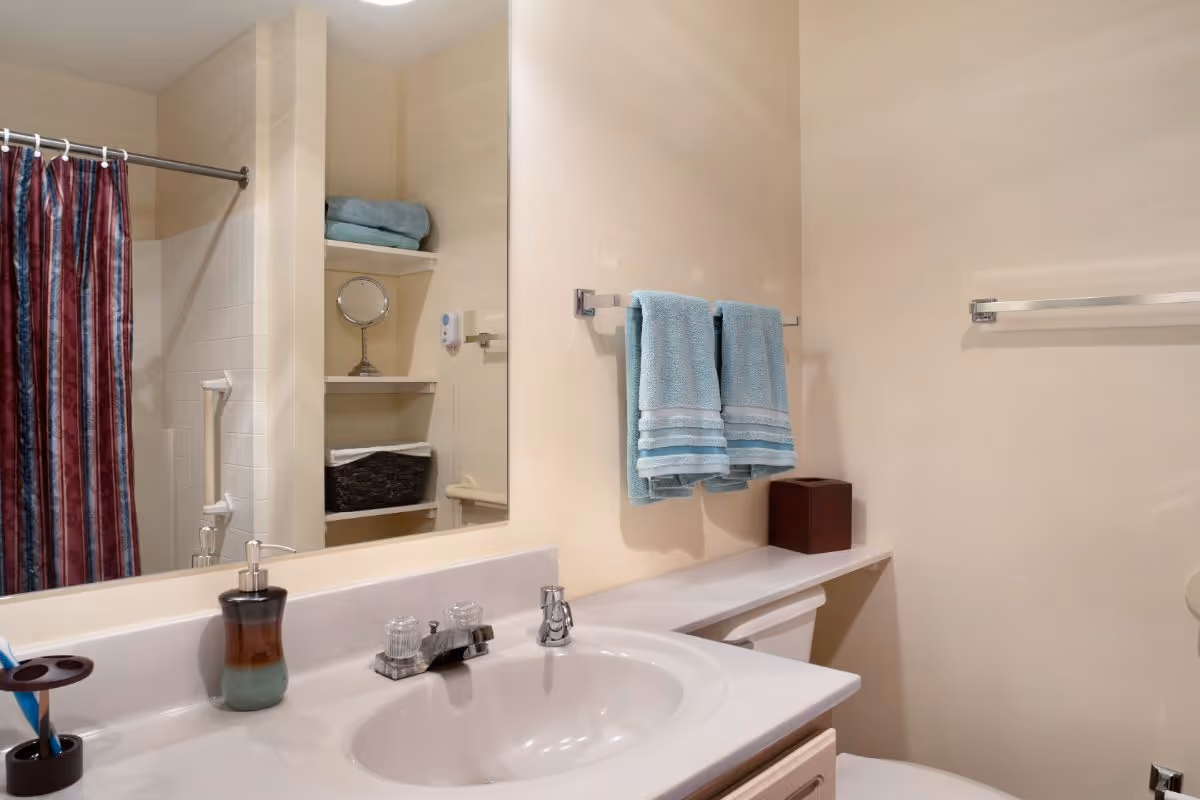 Bathroom with a sink and mirror, blue hand towels on a rack, and a shower with a striped curtain.