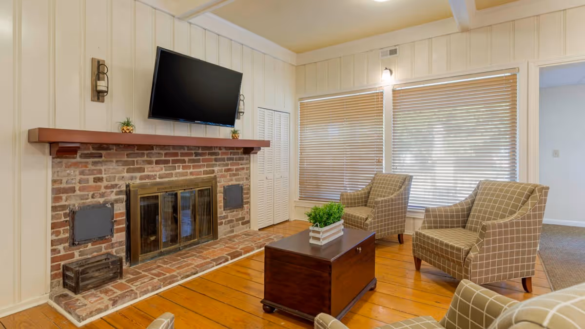 Cozy living room with a brick fireplace, wall-mounted TV, three upholstered armchairs, and a wooden coffee table.