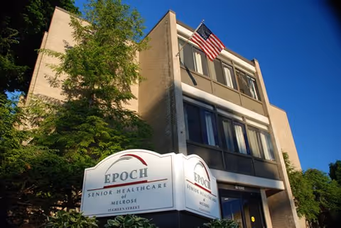 Entrance of a multi-story senior healthcare building with an American flag and a sign reading 'EPOCH Senior Healthcare of Melrose'.