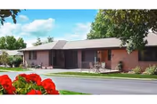 Single-story brick senior living building with patios and outdoor chairs, red flowers in the foreground and a blue sky above.