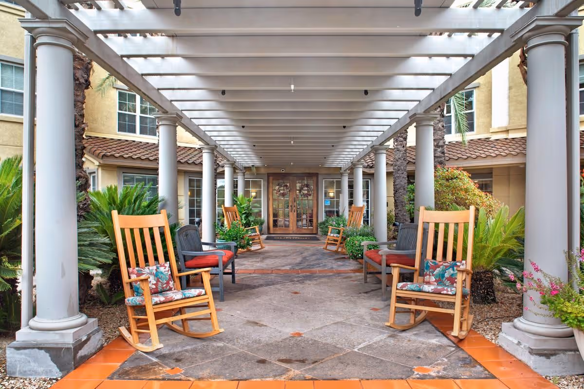 Covered front entrance patio with columns, rocking chairs, potted plants, and double doors in the background.