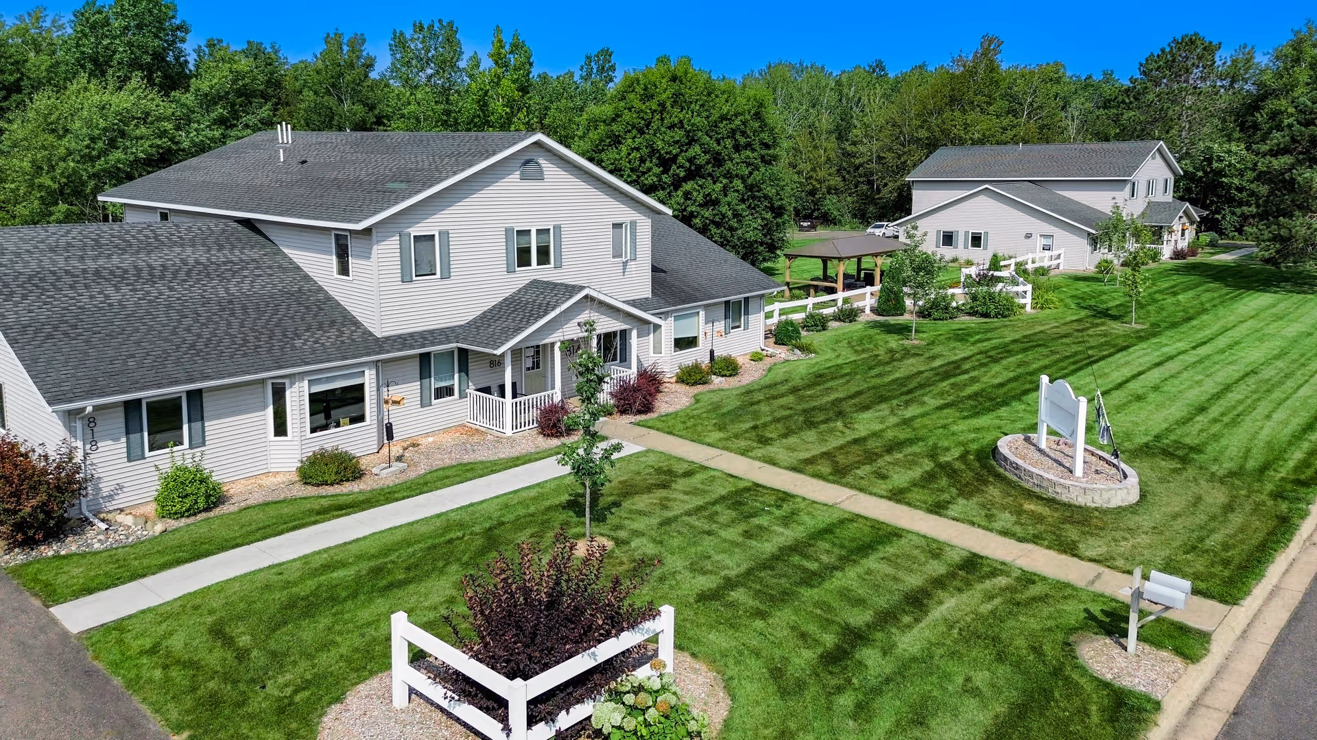 Aerial view of a residential senior living property with two light-colored buildings, manicured lawns, pathways, and a white entrance sign.