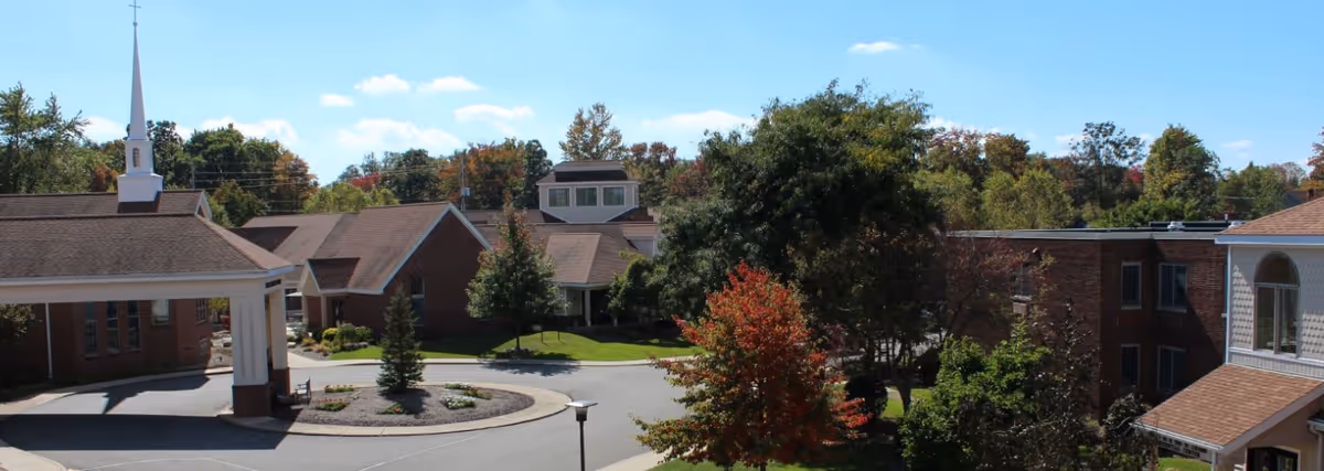 Front exterior view of the Wesbury United Methodist Community campus with brick buildings, a covered entrance with steeple, circular driveway and trees with fall foliage.
