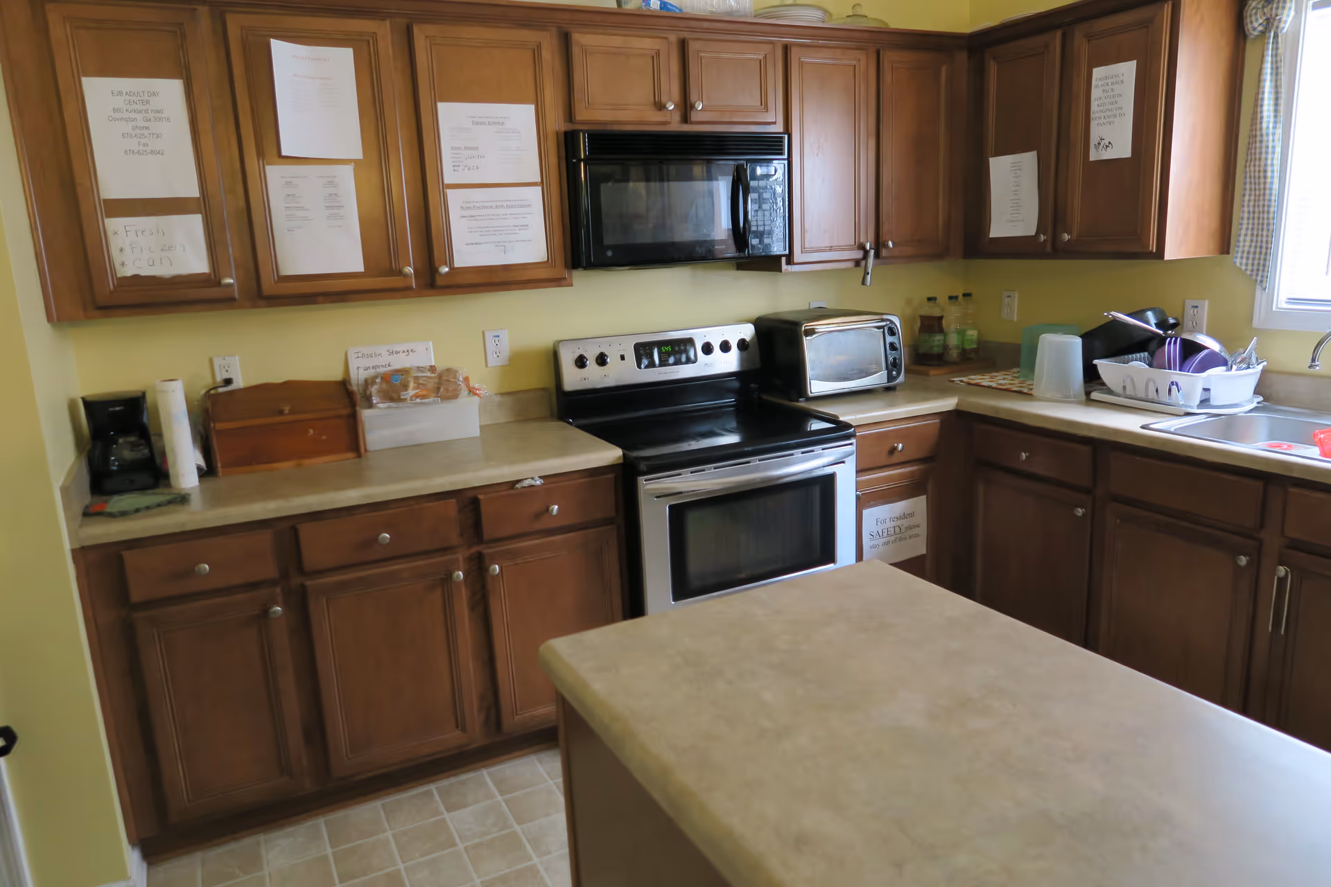 Small kitchen with wooden cabinets, stainless stove and microwave, toaster oven, sink, and a central island.