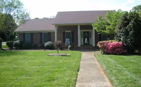 Front view of Grapperhall Family Care Home, a single-story brick facility with lawn and shrubs.