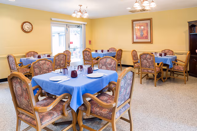 Dining room with several tables covered in blue tablecloths and upholstered chairs set for meals.