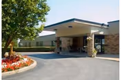 Front entrance of a senior living facility with a covered drop-off, brick columns, and landscaping.