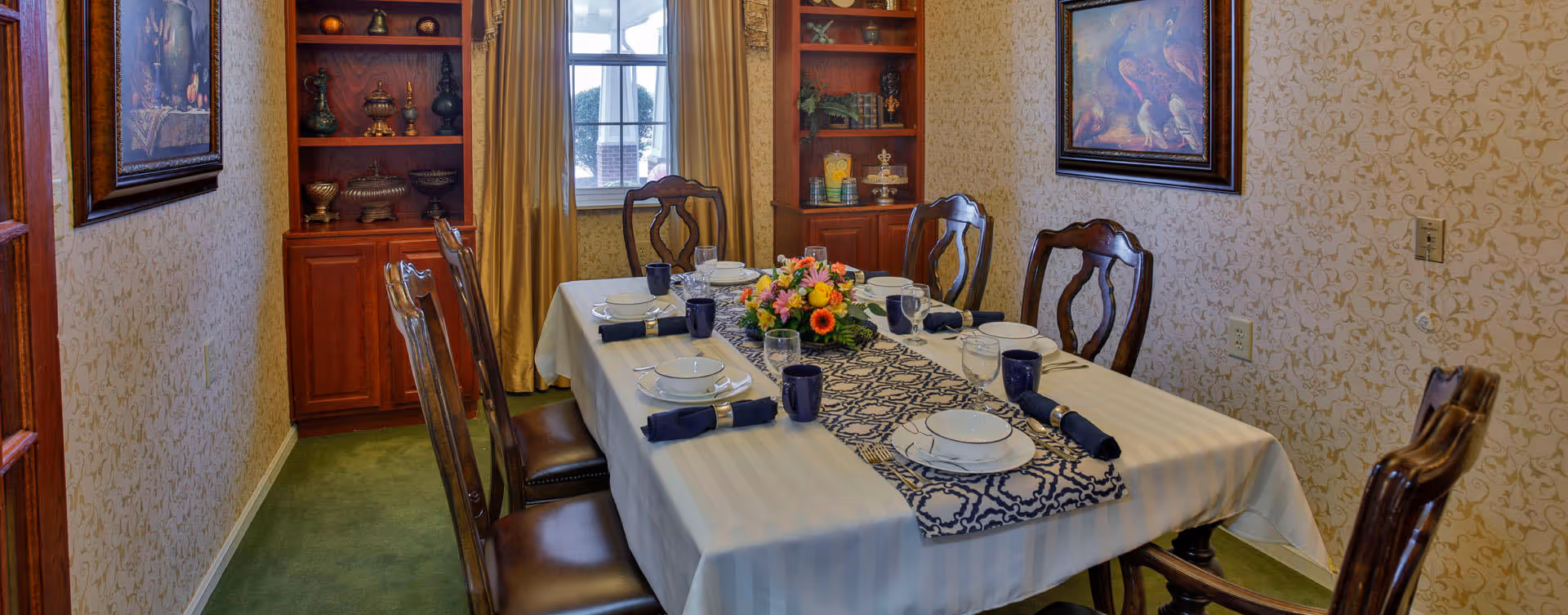 Formal dining room with a set table, floral centerpiece, wooden chairs, and built-in shelving by a window.