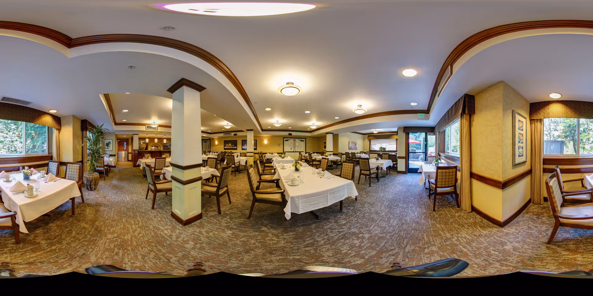Spacious dining room with multiple tables and chairs set for a meal, large windows, and warm lighting.