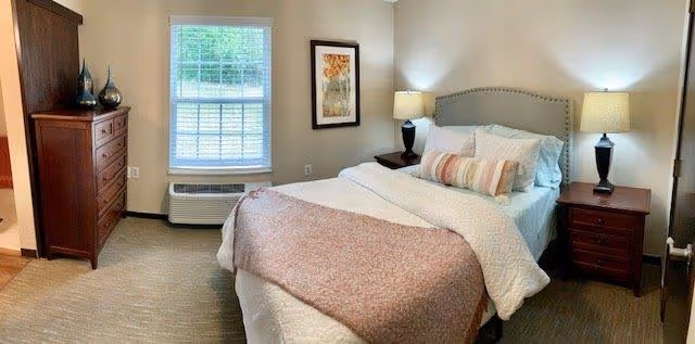 A neatly made bedroom with a double bed, two nightstands with lamps, a dresser, and a window.