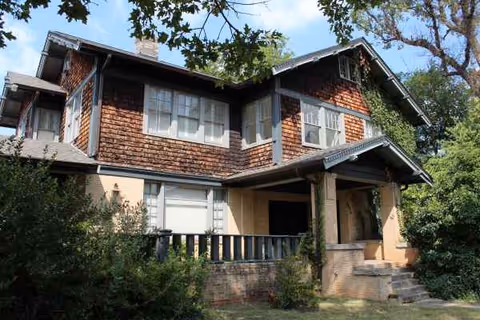 Two-story building with wood shingles, a front porch, and surrounding trees.