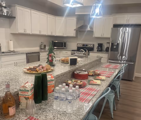 Bright modern communal kitchen with a long granite island laid out with drinks, snacks, and holiday decorations.