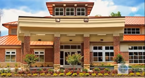 Front exterior view of Arden Courts of Richmond building with brick columns, large windows, a covered entrance, and a landscaped garden with shrubs and flowers in front.