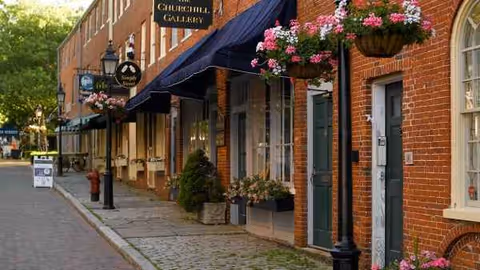 Brick storefronts line a cobblestone street with hanging flower baskets and awnings.