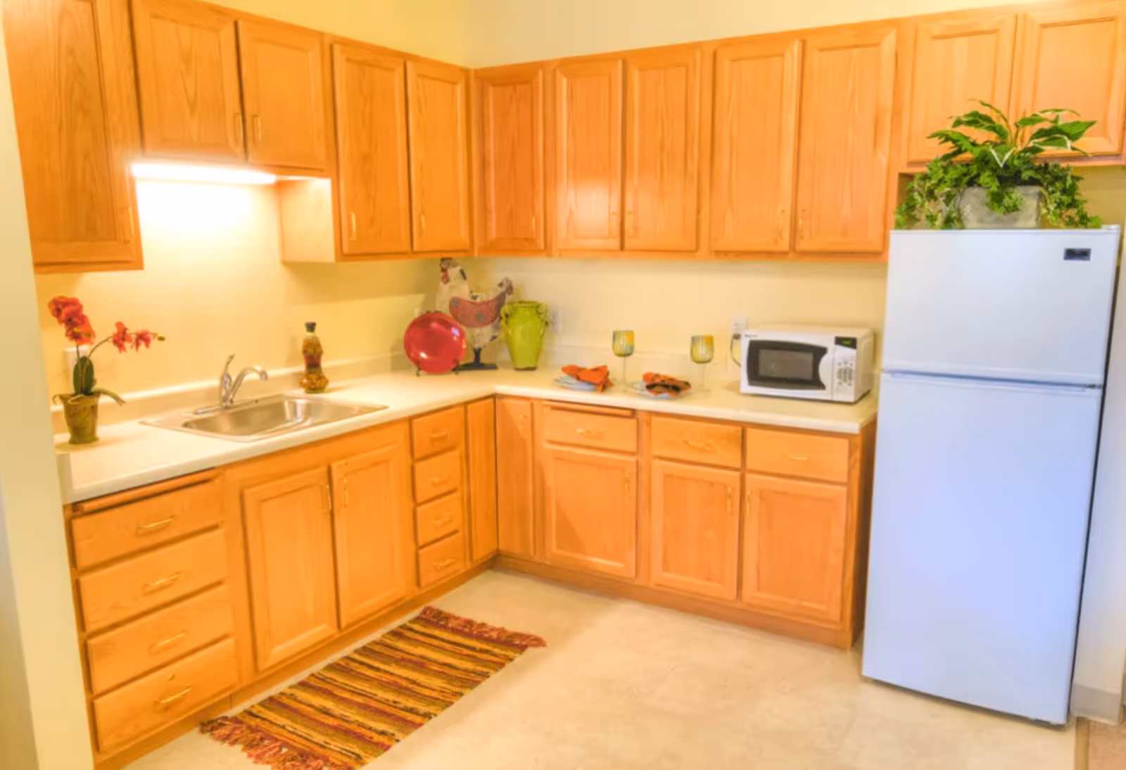 Bright kitchenette with oak cabinets, a sink, countertop microwave and decorative items next to a white refrigerator.