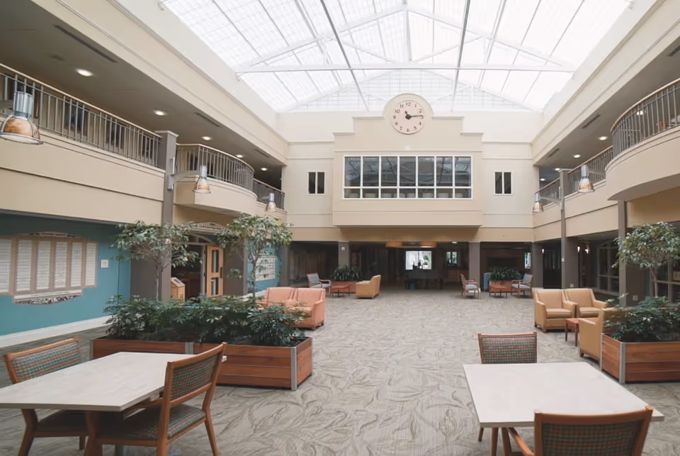 Spacious two-story atrium-style common area with seating, tables, plants, and a large skylight with a clock above.