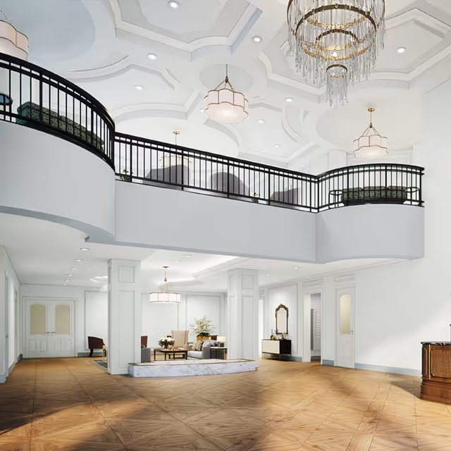 Spacious and elegant interior of a senior living facility with a high ceiling, decorative chandeliers, a mezzanine with black railings, and a seating area with chairs and a coffee table on a raised platform. The room features white walls, wooden flooring, and multiple doorways leading to other areas.