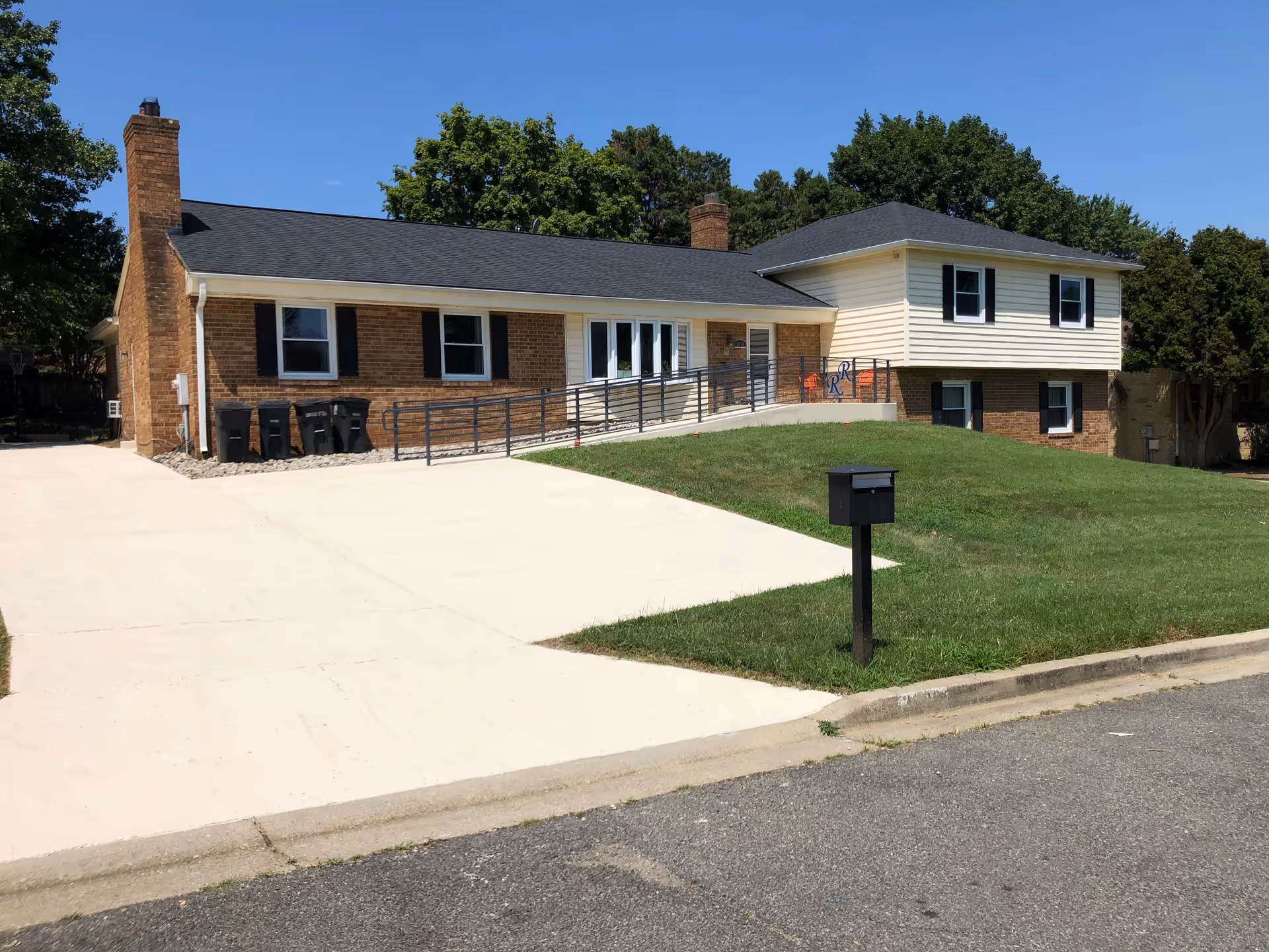 Front exterior of a brick-and-siding assisted living home with a wheelchair ramp, driveway, and mailbox.