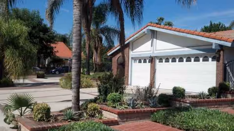 Front exterior of Genesis Manor IV with palm trees, brick planters, and a two-car garage.