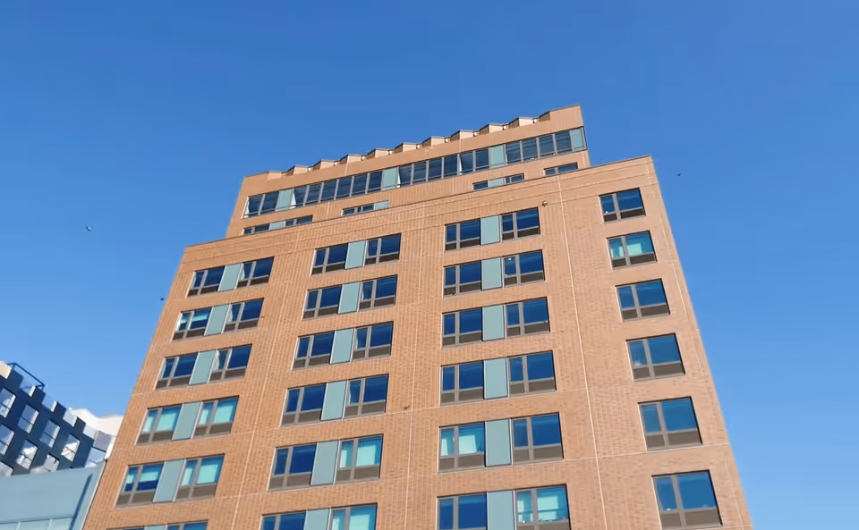 Tall multi-story brick building with many windows under a clear blue sky.