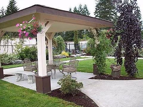 An outdoor pavilion with metal chairs and hanging flower baskets.