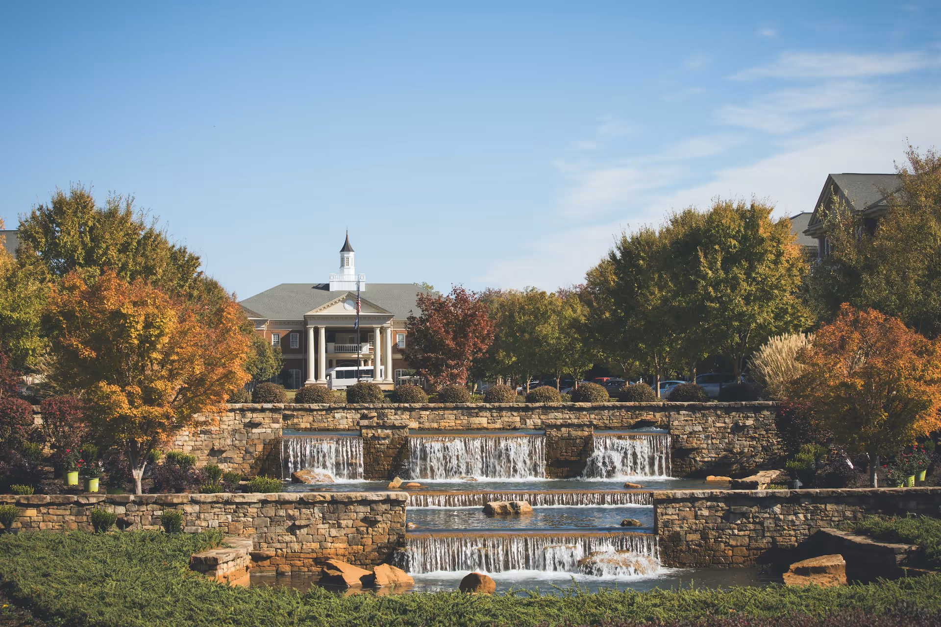 Front view of a stately building behind tiered stone waterfalls and autumn trees.