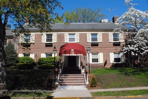 Front view of a brick building with a red awning and steps.
