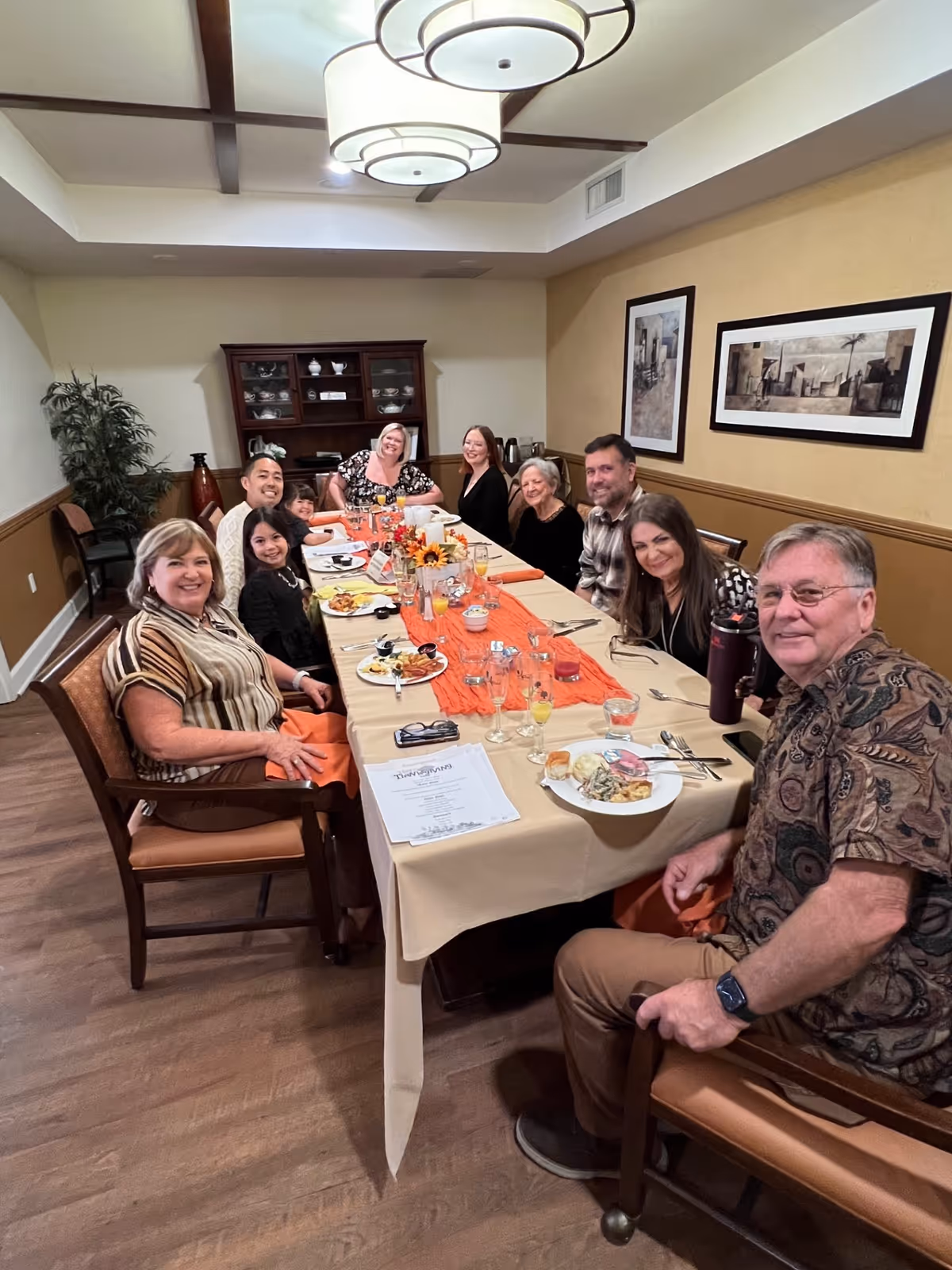 A group of people seated and smiling around a long, decorated dining table in a cozy private dining room.