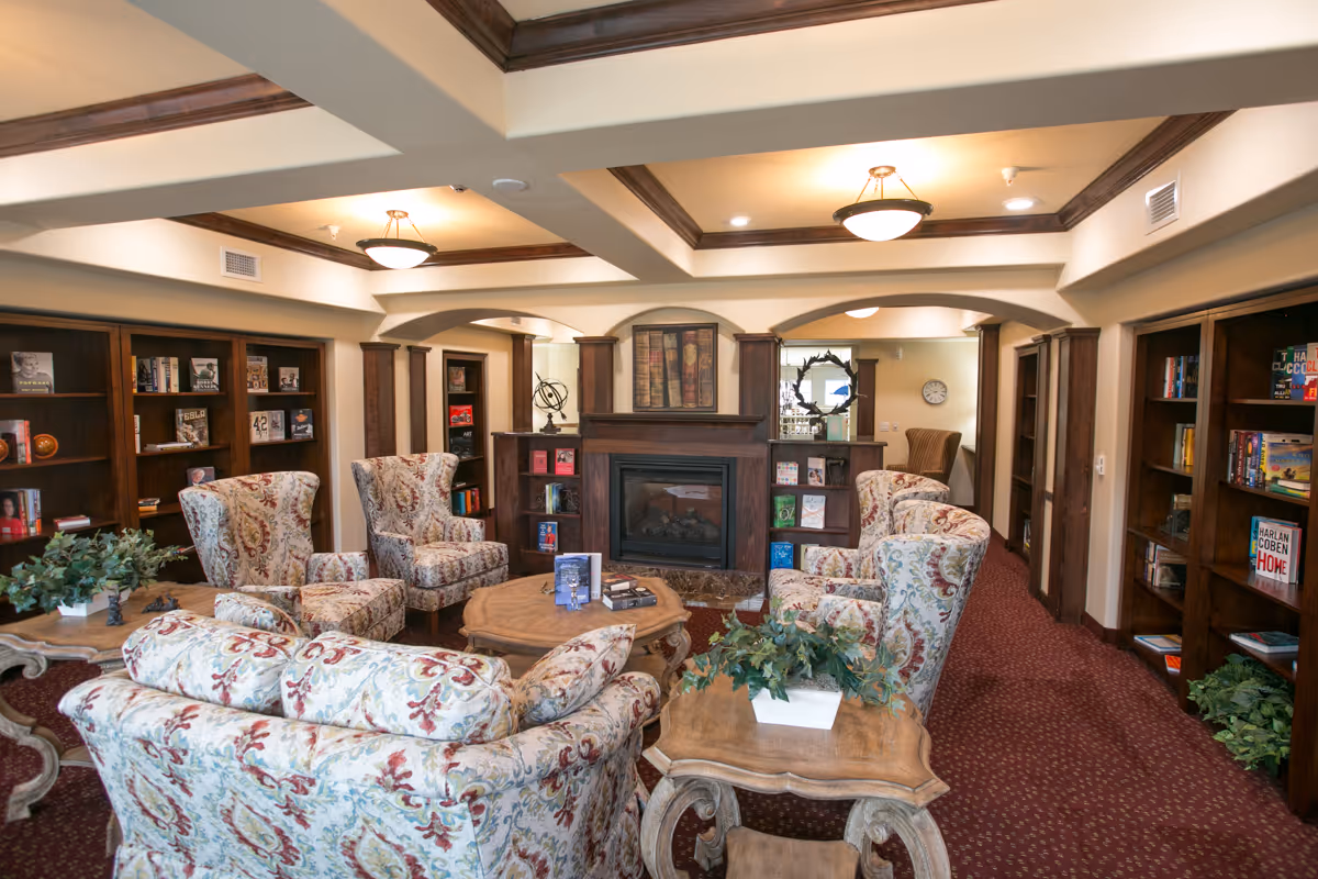 Cozy communal sitting room with patterned armchairs arranged around a coffee table facing a fireplace and built-in bookshelves.
