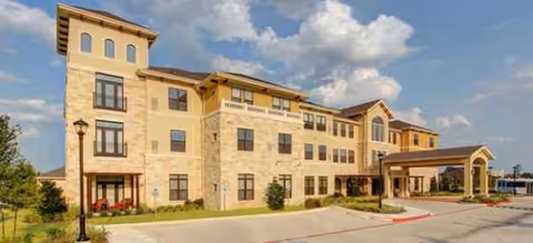 Exterior view of a multi-story stone senior living building with a covered entrance.