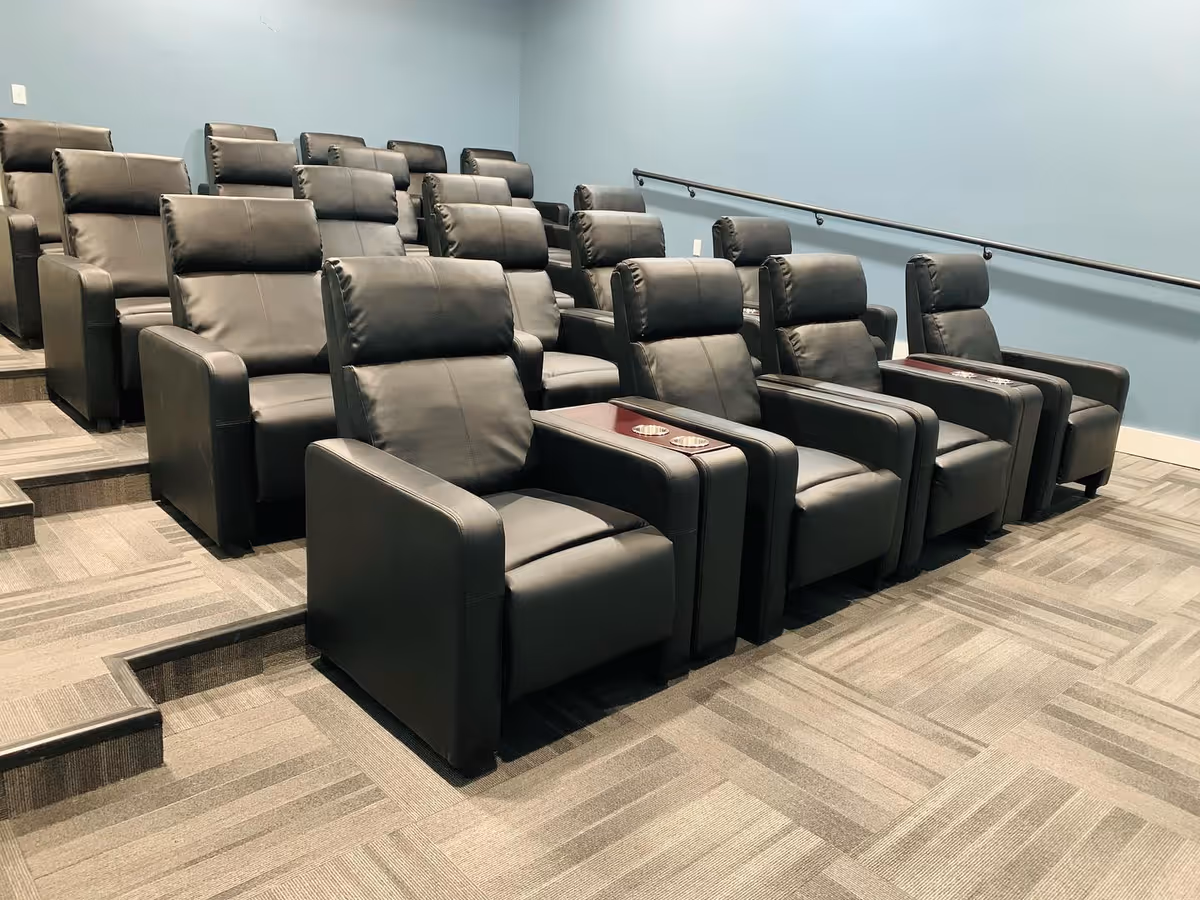 Tiered small theater room with rows of black leather recliner chairs and cupholders against a blue wall.