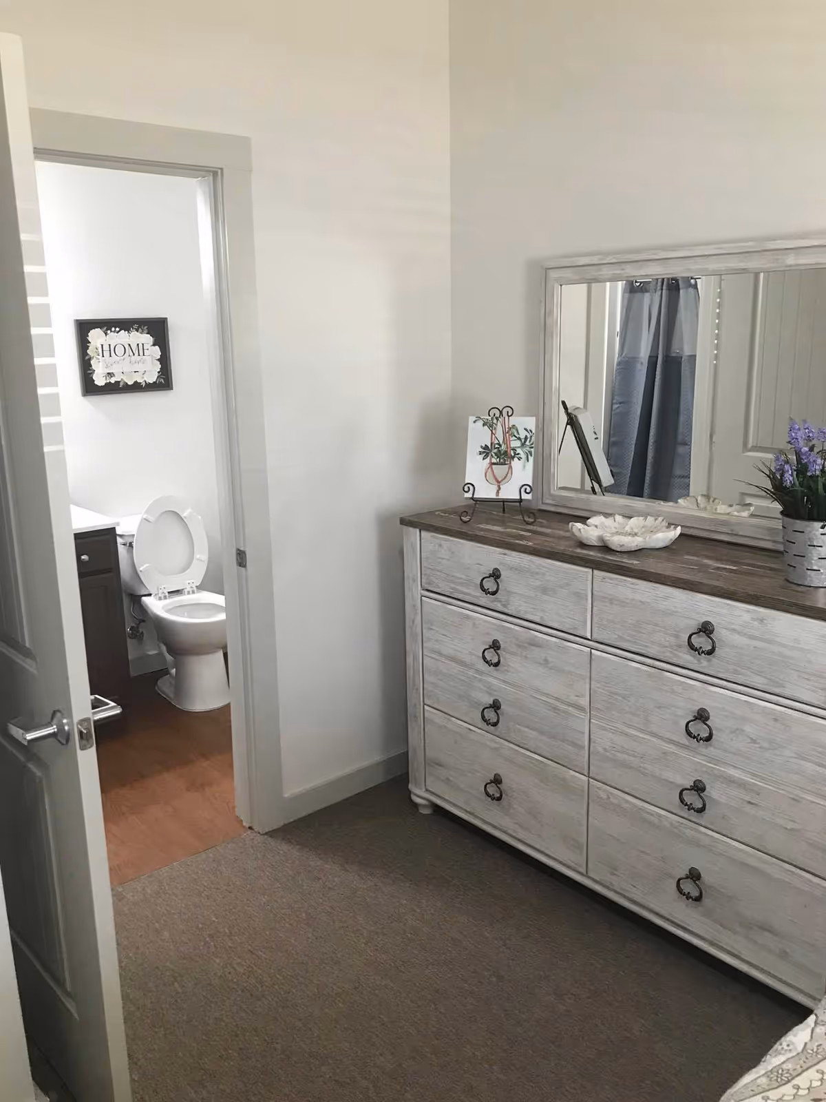 Bedroom with a whitewashed dresser and mirror, and an open door revealing a bathroom with a toilet.