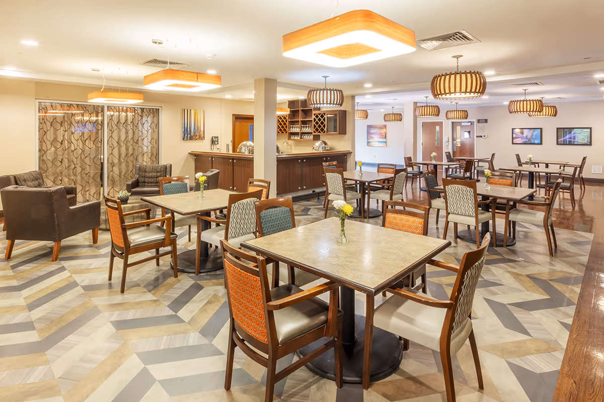 A spacious, well-lit dining area with multiple tables and chairs and a beverage bar in the background.