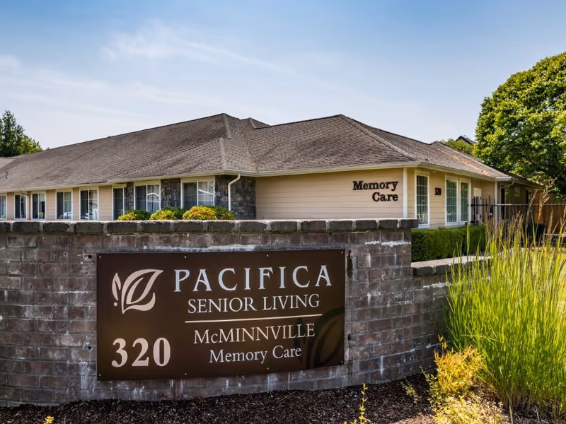 Exterior view of the Pacifica Senior Living McMinnville Memory Care building with a brick entrance sign reading Pacifica Senior Living 320 McMinnville Memory Care.