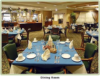 A dining room with multiple tables set with blue tablecloths, folded napkins, place settings and chairs.